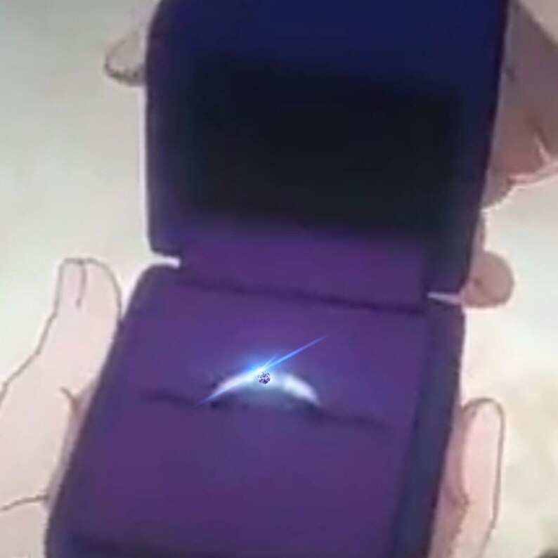 May include: A purple velvet ring box with a silver ring and a blue gemstone in the center.