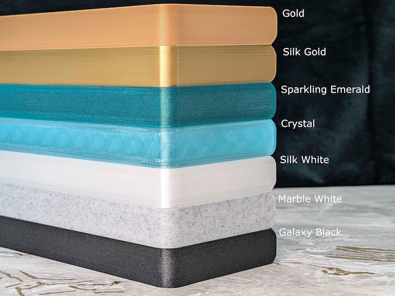 May include: A stack of rectangular blocks in various colors, including gold, silk gold, sparkling emerald, crystal, silk white, marble white, and galaxy black. Each block is labeled with its color name.