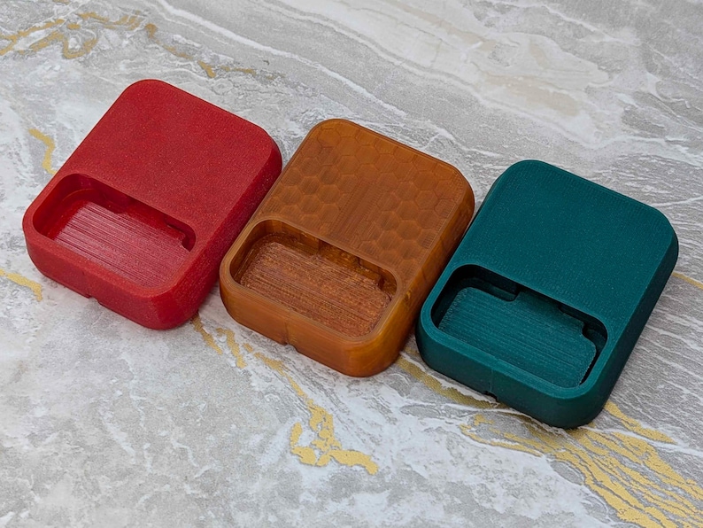 May include: Three rectangular, open-top containers in red, brown, and teal. The containers have a recessed area on one side. The brown container has a textured, honeycomb-like pattern. The containers are arranged side by side.