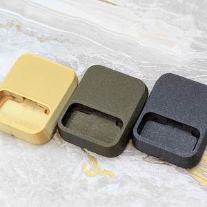 May include: Three rectangular, textured cases in a row. The cases are in shades of yellow, olive green, and dark gray. Each case has a rectangular cutout on one side. The cases are on a light-colored, patterned surface.