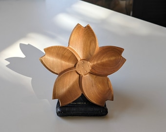 May include: A wooden cherry blossom-shaped dish with five petals. The dish is made of light brown wood and has a smooth, polished finish.