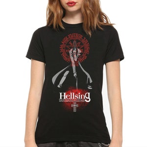 May include: A black short-sleeve t-shirt featuring a graphic of a character in a long coat holding a sword. Above the character is a red circular seal with text. Below is the word Hellsing, a cross, and the text: In the name of God, impure souls of the living dead shall be banished into eternal damnation. Amen.