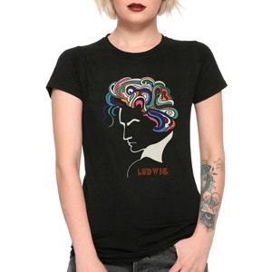 Op de afbeelding: Zwart t-shirt met een profiel van een persoon met kleurrijk, abstract haar. Het woord "LUDWIG" is in bruin gedrukt. Een grafisch en artistiek ontwerp.