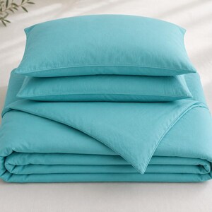 Turquoise cotton duvet cover set styled in a bright coastal bedroom with matching pillow covers, wooden furniture, beach wall art, and natural sunlight.