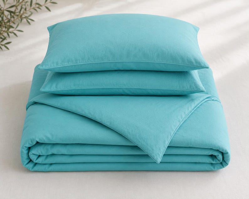 Turquoise cotton duvet cover set styled in a bright coastal bedroom with matching pillow covers, wooden furniture, beach wall art, and natural sunlight.