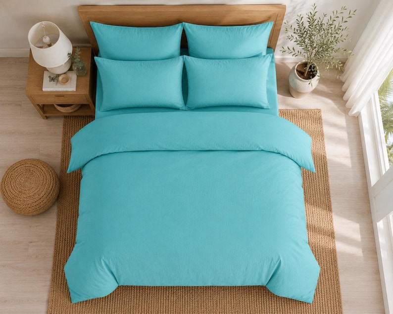 Turquoise cotton duvet cover set styled in a bright coastal bedroom with matching pillow covers, wooden furniture, beach wall art, and natural sunlight.