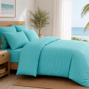 Turquoise cotton duvet cover set styled in a bright coastal bedroom with matching pillow covers, wooden furniture, beach wall art, and natural sunlight.