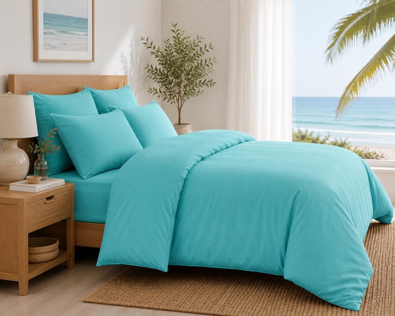 Turquoise cotton duvet cover set styled in a bright coastal bedroom with matching pillow covers, wooden furniture, beach wall art, and natural sunlight.