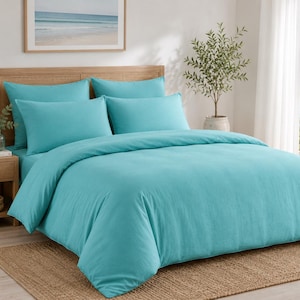Turquoise cotton duvet cover set styled in a bright coastal bedroom with matching pillow covers, wooden furniture, beach wall art, and natural sunlight.