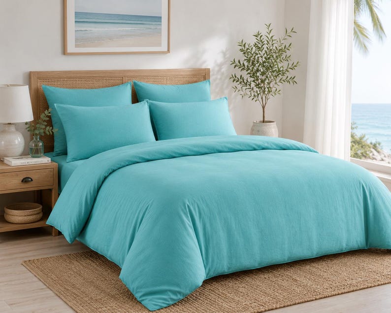 Turquoise cotton duvet cover set styled in a bright coastal bedroom with matching pillow covers, wooden furniture, beach wall art, and natural sunlight.