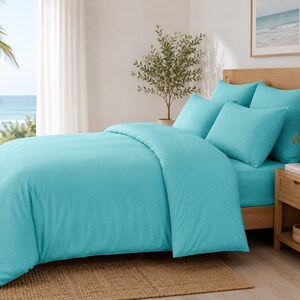 Turquoise cotton duvet cover set styled in a bright coastal bedroom with matching pillow covers, wooden furniture, beach wall art, and natural sunlight.