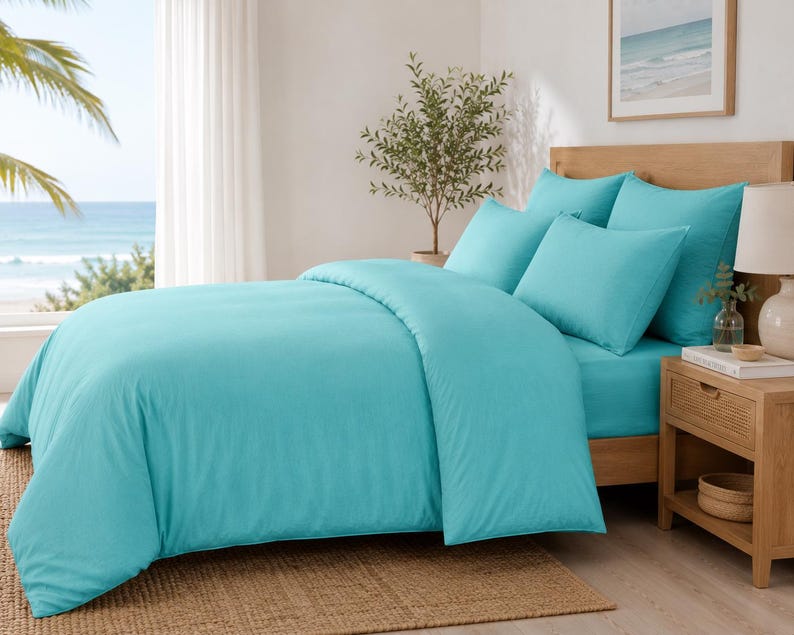 Turquoise cotton duvet cover set styled in a bright coastal bedroom with matching pillow covers, wooden furniture, beach wall art, and natural sunlight.