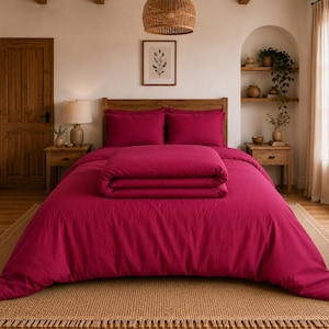 Pode incluir: Um conjunto de roupa de cama em magenta vibrante, incluindo uma capa de edredão e duas fronhas a condizer. A cama está arrumada com um edredão dobrado sobre a capa principal, apresentando uma cor rosa profunda e um tecido texturizado.