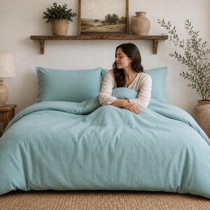 Pode incluir: Um conjunto de capa de edredão azul-claro sólido com um par de fronhas retangulares a condizer. A roupa de cama é feita de um tecido texturizado e está estendida sobre uma cama, proporcionando um aspeto limpo e uniforme.