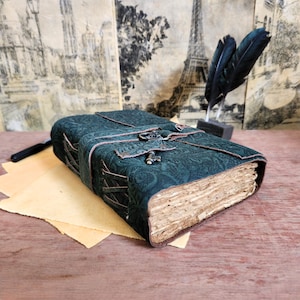 May include: A dark green leather-bound journal with a keyhole and a decorative key. The journal has a paisley pattern and is tied with brown leather straps.