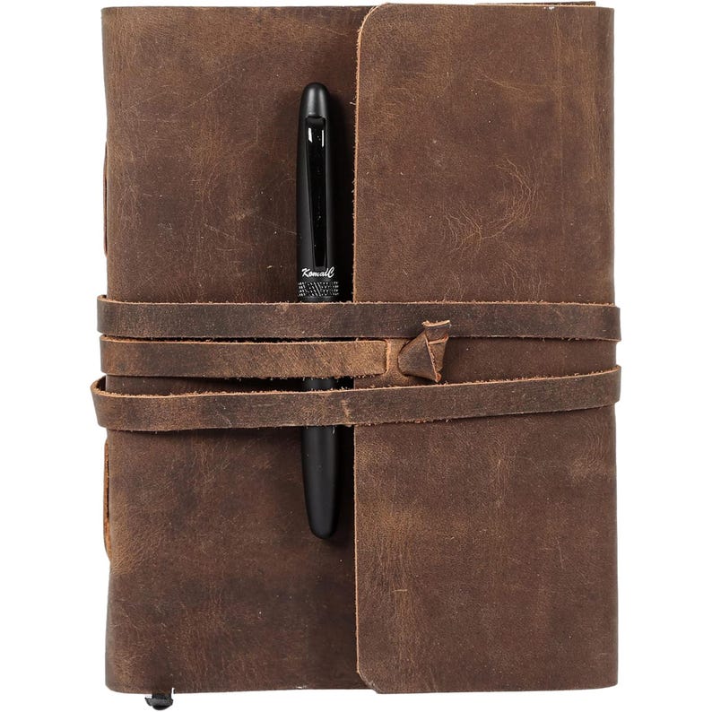 Puede incluir: Un diario de cuero marr&oacute;n con un bol&iacute;grafo metido en la correa de cuero. El diario tiene un aspecto desgastado y est&aacute; cerrado.