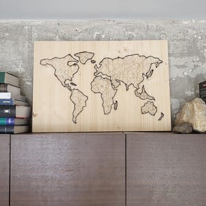 Könnte beinhalten: Eine Weltkarte aus Holz mit einem String-Art-Design. Die Karte ist auf einem hellbraunen Holzrahmen montiert und wird in einem Regal mit Büchern ausgestellt.