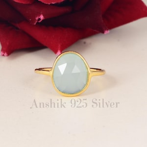 May include: A silver ring with a gold-plated finish and a light blue gemstone. The ring is set on a white background.