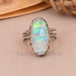 May include: A silver ring featuring a large oval opal gemstone. The ring has a delicate, twisted band and an intricate setting around the stone.
