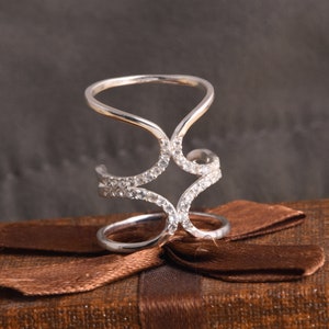 Può includere: Un anello d'argento con un delicato design traforato che presenta una stella centrale. L'anello è adornato con piccole pietre preziose trasparenti.