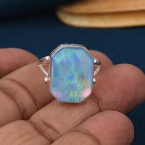 May include: A silver ring featuring a large, faceted, iridescent blue opal gemstone. The ring has a simple, elegant design.