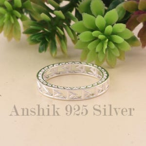 Puede incluir: Un anillo de plata con un diseño geométrico de triángulos y líneas. El anillo se encuentra sobre un fondo de follaje verde y morado. El texto "Anshik 925 Silver" es visible.