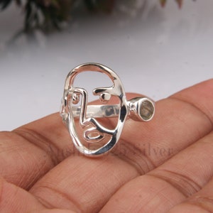 May include: Silver ring with a face cutout design and a light blue gemstone.