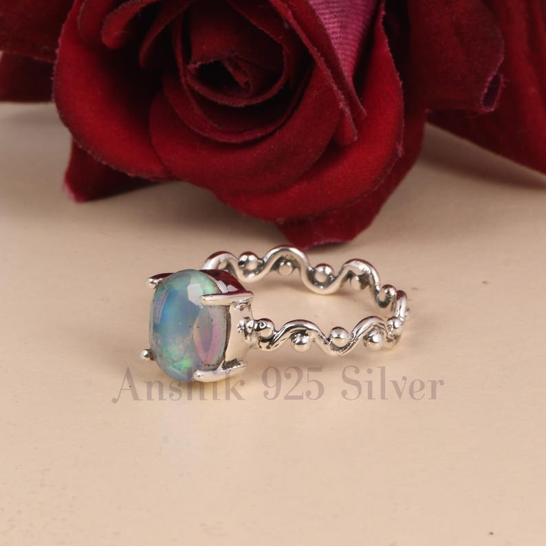 K&ouml;nnte beinhalten: Ein silberner Ring mit einem ovalen, schillernden Opal-Edelstein. Das Band hat ein dekoratives, wellenf&ouml;rmiges Design. Der Text "Anshik 925 Silver" ist auf dem Ring zu sehen.
