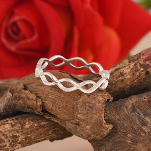 May include: A silver ring with a delicate, interwoven design. The ring is made of a smooth, polished metal and has a simple, elegant style.