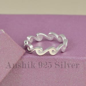 May include: A silver ring featuring a continuous wave pattern design. The band is crafted from polished metal and displays a repeating series of interconnected crests. The text "Anshik 925 Silver" is visible in the lower portion of the image.