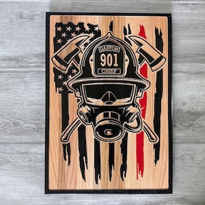 May include: A wooden plaque with a black and red American flag design. A firefighter's helmet with a gas mask is superimposed on the flag. The helmet has the text "GASTON 901 CHIEF" on it.