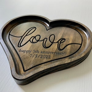 May include: A heart-shaped wooden tray with a dark brown stain. The tray is engraved with the word "love" in a cursive font and the text "happy 5th anniversary! 7/3/2022".