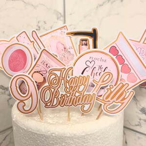 May include: Pink and gold cake toppers with the words "Happy Birthday Lilly" and various makeup and beauty themed designs.