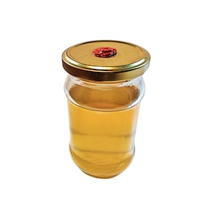Può includere: Un barattolo di vetro con un coperchio dorato e un sigillo rosso riempito di un liquido giallo chiaro.