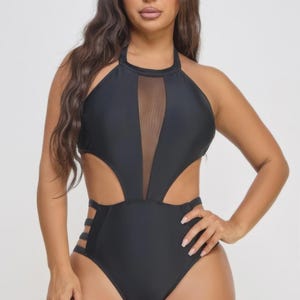 May include: A black halter-neck swimsuit with a mesh panel at the bust and cut-out detailing. The one-piece swimsuit features cut-outs at the waist and sides, and straps on the hips. The swimsuit is a solid black color.