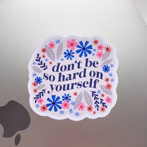 Puede incluir: Una pegatina blanca con un borde floral y el texto "no seas tan duro contigo mismo".