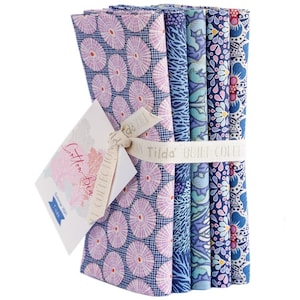 Könnte beinhalten: Ein Bündel gemusterter Stoffquadrate, gebunden mit einem cremefarbenen Band. Die Stoffe zeigen verschiedene blaue und violette Blumen- und geometrische Designs. Ein Etikett lautet "Cotton Beach Summer 2021 Tilda QUILT COLLECTION."