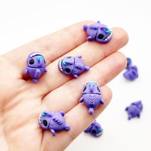 以下が含まれることがあります： 紫色の小さなアンコウのフィギュアのコレクション。各魚は質感のある体、白い歯が見える目立つ口、黒い目、そして額から伸びる小さなティール色のルアーが特徴です。フィギュアは明確なヒレと丸みを帯びた形状で成形されています。