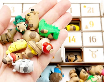 Op de afbeelding: Een verzameling kleine, veelkleurige dierenfiguurtjes, waaronder een groene dinosaurus, een geel wezen en een figuurtje met een rode muts, vastgehouden in een handpalm. Op de achtergrond staat een bruin-witte adventskalender met genummerde deurtjes.