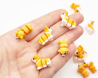 Op de afbeelding: Kleine, beweegbare corgi-figuurtjes in een geel en wit kleurenschema met zwarte ogen en neuzen. Deze miniatuur hondjes hebben gesegmenteerde lichamen die beweging mogelijk maken en worden in een groep getoond.