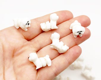 Op de afbeelding: Een verzameling kleine, witte, hondvormige beeldjes gemaakt van een glad materiaal. Elke miniatuurhond heeft een afgerond lichaam, een klein staartje en een opvallende zwarte neus en zwarte ogen, in een staande of zittende houding.