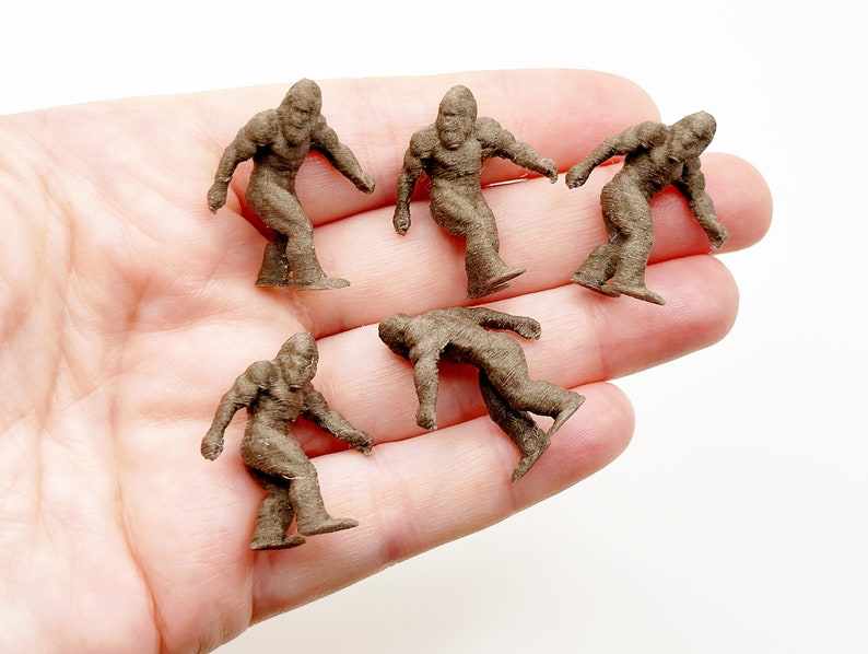 May include: Six brown miniature figurines of Bigfoot, each standing upright with arms outstretched, on a person's hand.