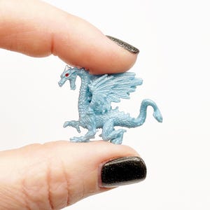 Peut inclure: Une petite figurine de dragon en plastique bleu clair avec des yeux rouges. Le dragon a des ailes et une longue queue.