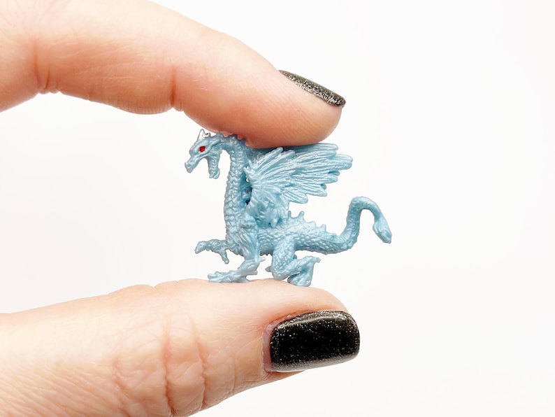 Peut inclure: Une petite figurine de dragon en plastique bleu clair avec des yeux rouges. Le dragon a des ailes et une longue queue.