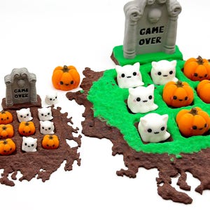 May include: A Halloween diorama with miniature orange pumpkins and white ghost figures on a brown base with green accents. A grey tombstone with "GAME OVER" is also present. The scene is set against a white background.
