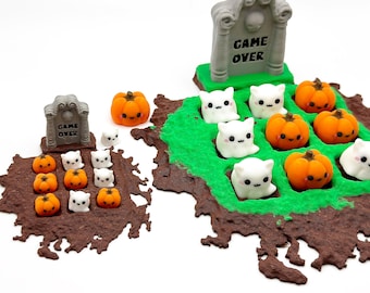 May include: A Halloween-themed diorama featuring miniature orange pumpkins and white ghost figures arranged on a brown base with green accents. A gray tombstone with the words "GAME OVER" is also present. The scene is set against a white background.
