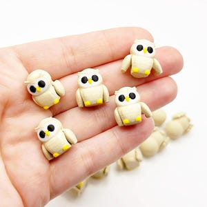 Peut inclure: Une collection de petites figurines de hiboux blanches avec des becs jaunes et des yeux noirs. Les hiboux sont disposés sur une main, certains hiboux faisant face à l'avant et d'autres de côté.