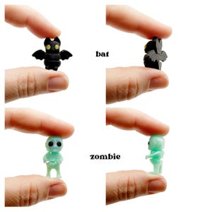 Peut inclure: Une petite figurine de chauve-souris noire aux yeux jaunes et une petite figurine de zombie vert clair translucide aux yeux noirs. La chauve-souris est &eacute;tiquet&eacute;e avec le texte bat et le zombie avec le texte zombie, vus de face et de profil.