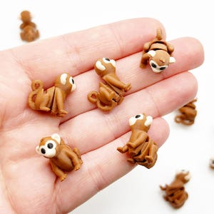 May include: A hand holding a collection of small brown monkey figurines. The monkeys have white eyes and are made of a smooth, brown material.