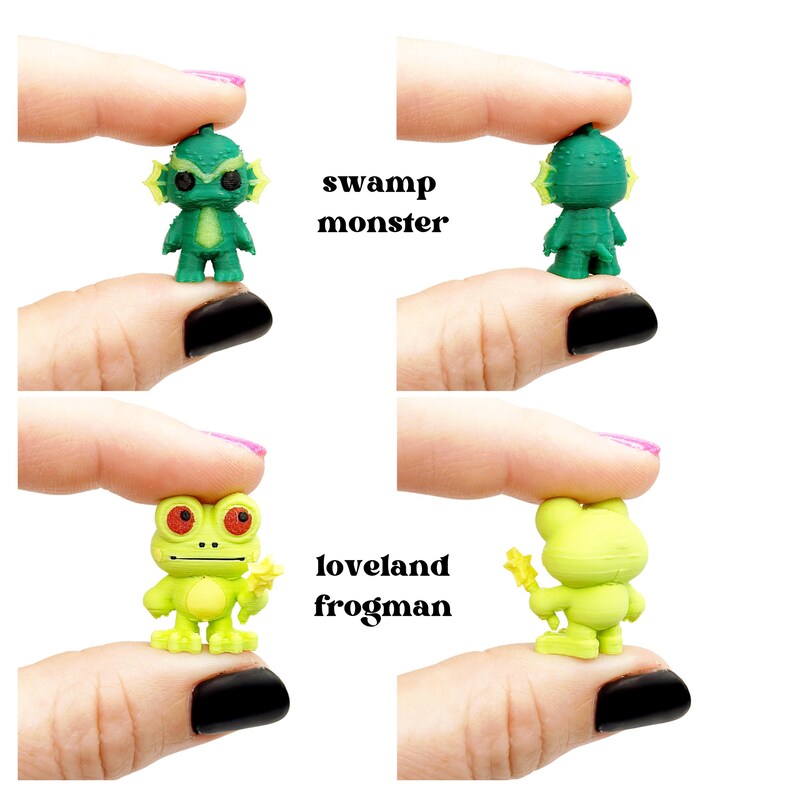 May include: Miniature green Swamp Monster and Loveland Frogman figurines. The Swamp Monster has a textured head and yellow gills. The Loveland Frogman is light green with red eyes and a yellow star. Text reads "swamp monster" and "loveland frogman".